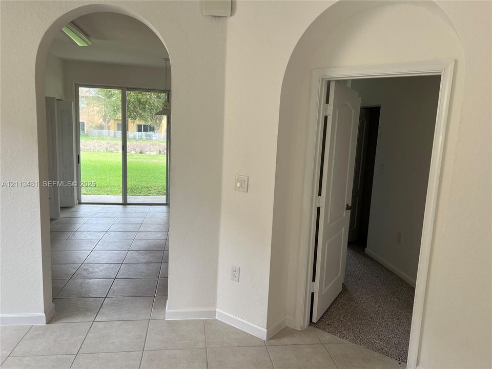 Interior featuring dual arched doorways, neutral ceramic tile flooring, sliding glass patio doors, and paneled interior doors