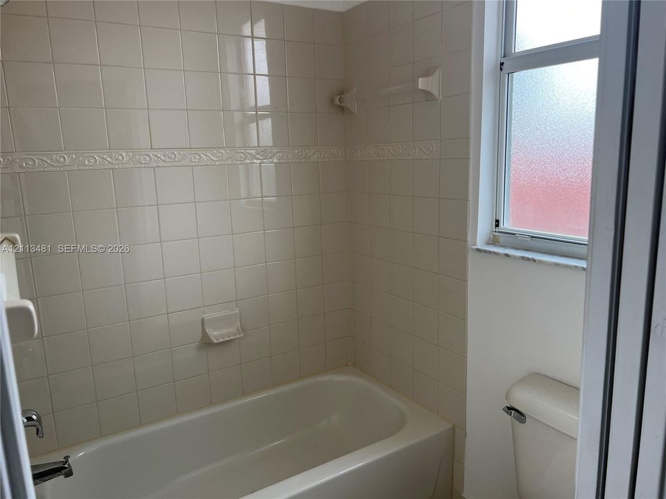 Bathtub with a built-in soap dish and decorative tile surround, completed by a window with privacy glass and a two-piece toilet