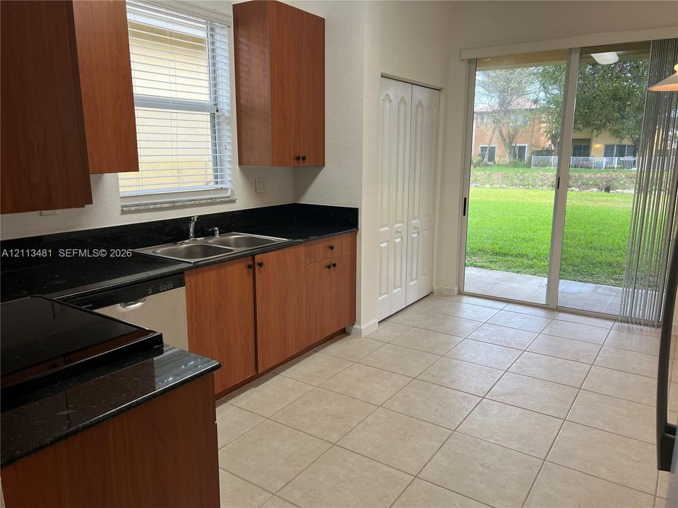 Kitchen featuring wood-finish cabinetry, dark solid-surface countertops, double-basin stainless steel sink, tile flooring, and sliding glass doors