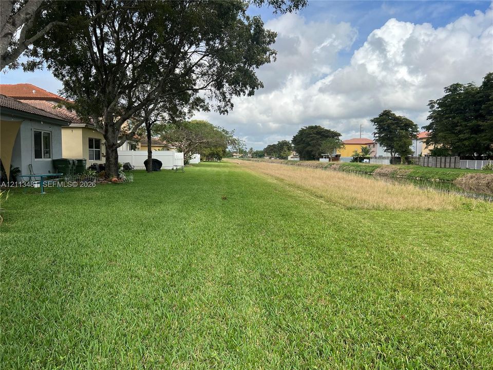 Expansive backyard featuring a grass lawn, mature trees, white privacy fencing, and direct water frontage