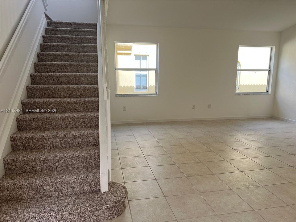 Interior space featuring neutral wall-to-wall ceramic tile flooring, a carpeted staircase with a white handrail, and two large windows