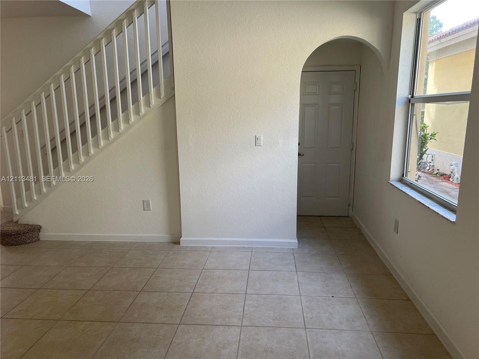 Entryway featuring neutral tile flooring, a staircase with white vertical balusters, a paneled door, and an arched doorway
