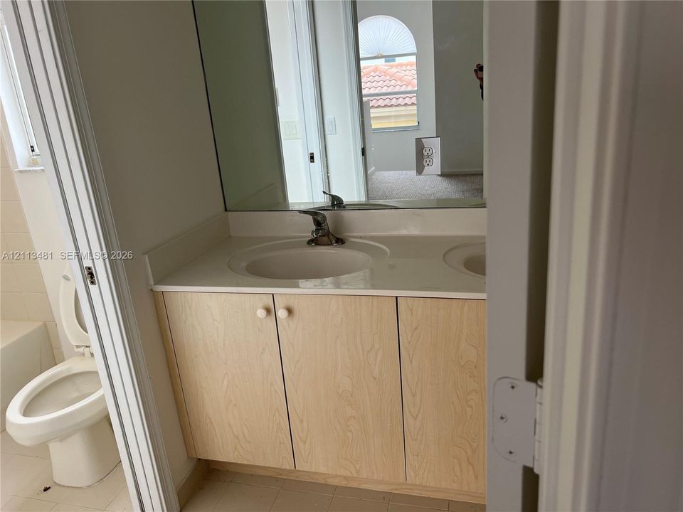 Bathroom vanity featuring light-toned wood-finish cabinetry, a solid-surface countertop with an integrated basin, a polished chrome single-handle faucet, and a large frameless wall-mounted mirror