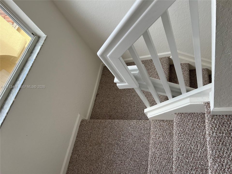 Staircase featuring wall-to-wall carpeting, white painted wooden balusters, and a rectangular window