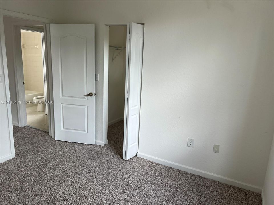 Neutral-toned wall-to-wall carpeting, white interior doors with brass-finish hardware, and built-in closet storage