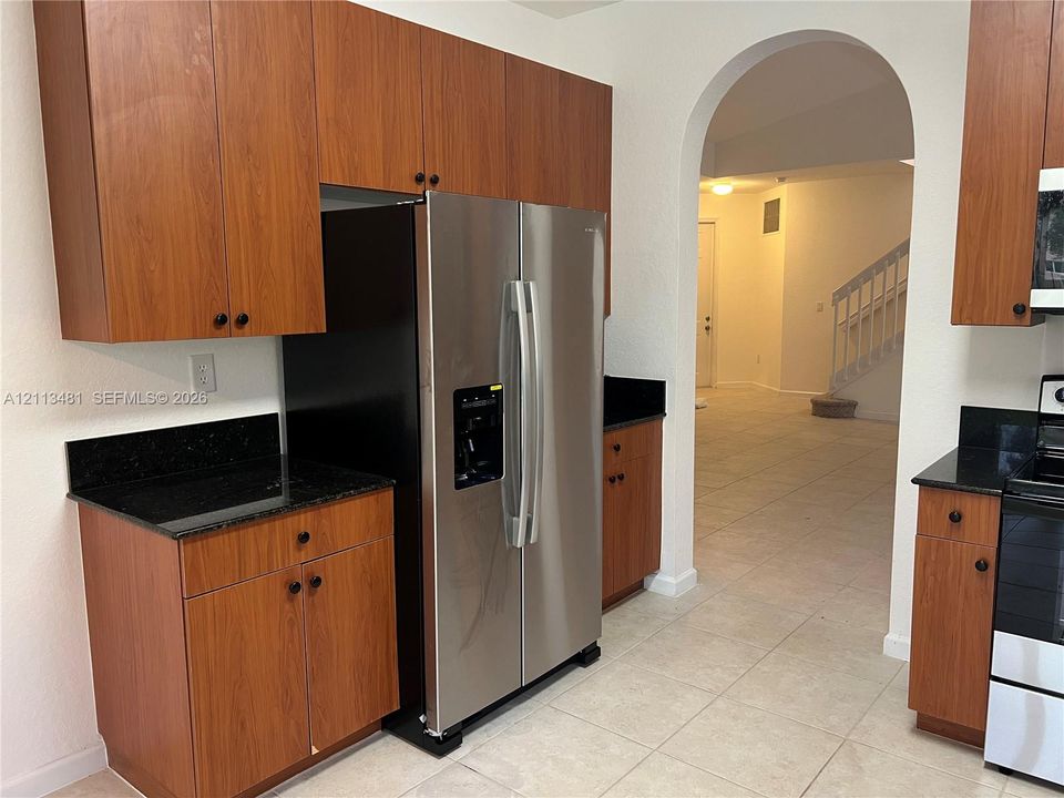 Kitchen featuring wood-finish cabinetry, dark stone countertops, stainless steel side-by-side refrigerator, and tile flooring