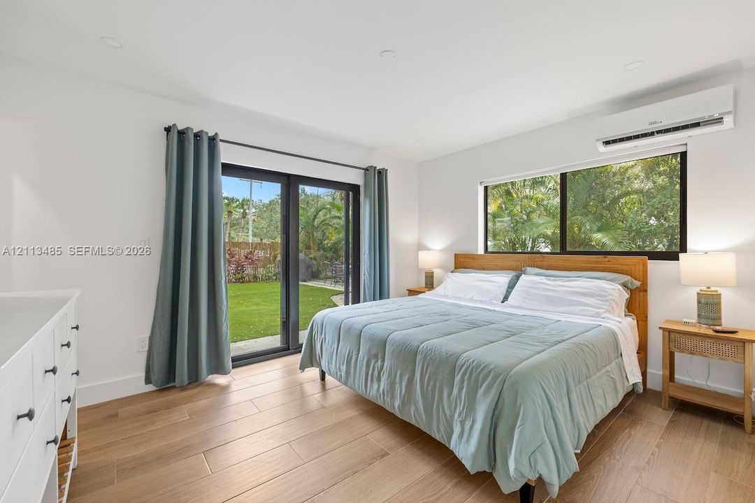 Light-filled room featuring wood-finish flooring, recessed lighting, a wall-mounted ductless air conditioning unit, and sliding glass doors with dark frames