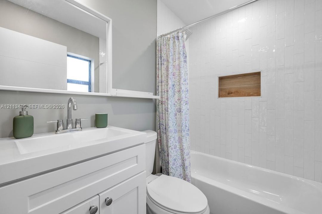 Bathroom featuring a white vanity with integrated basin, polished chrome faucet, rectangular wall mirror, white vertical subway tile surround, and built-in wood-finish shower niche