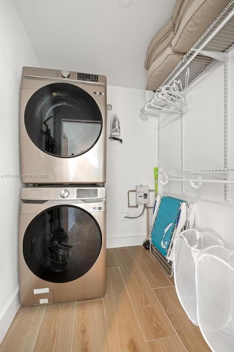 Laundry area featuring stacked appliances, wood-finish tile flooring, and integrated wire shelving