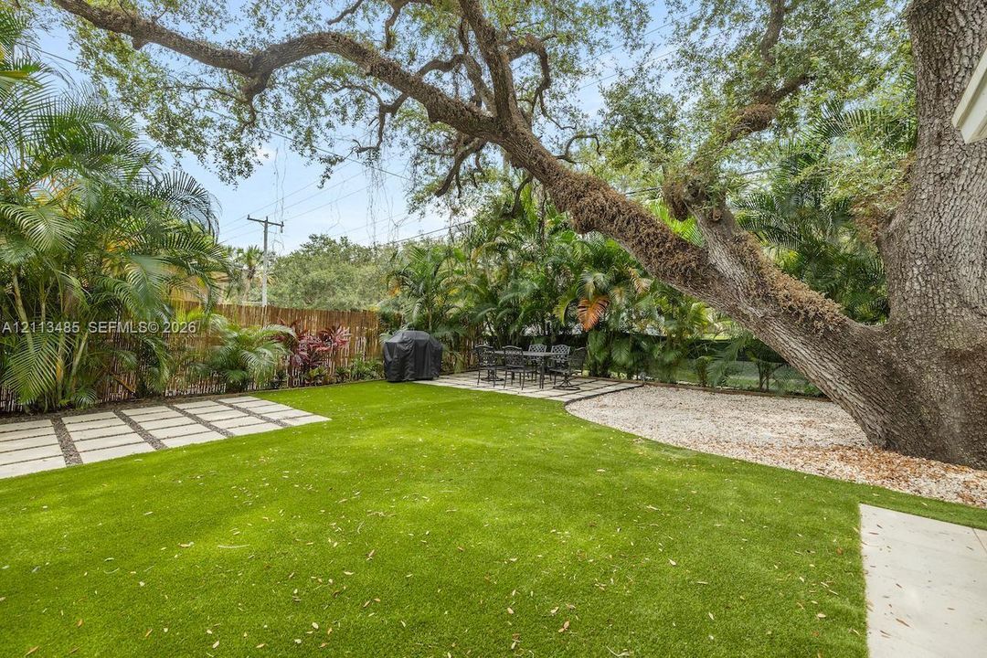 Backyard featuring synthetic turf, concrete paver accents, a gravel ground cover area, and mature canopy trees