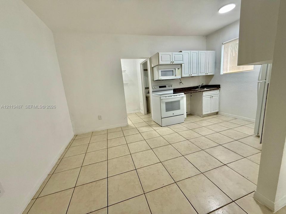 Kitchen featuring white cabinetry, solid-surface countertops, tile flooring, and integrated white appliances