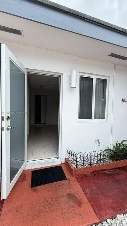 Exterior entry featuring a half-lite door, white stucco siding, dual-head cylinder wall sconce, and a decorative wrought-iron planter border
