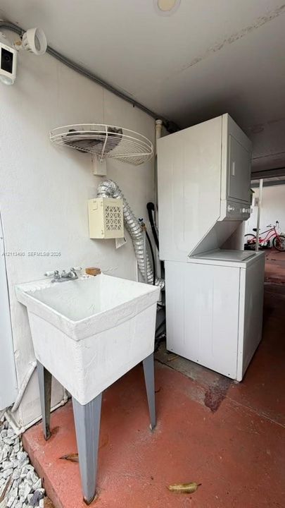Utility area featuring a floor-mounted basin with double-handle faucet, stackable laundry unit, wall-mounted wire shelving, and recessed ceiling lighting