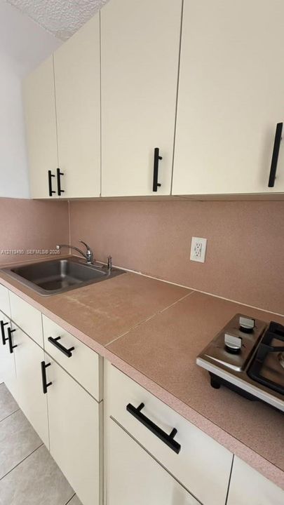 Kitchen featuring cream cabinetry, matte black hardware, solid surface countertops, a stainless steel drop-in sink, and a two-burner gas cooktop