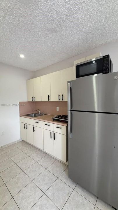 Kitchen featuring white cabinetry with matte black hardware, stainless steel refrigerator, built-in microwave, drop-in sink, and tile flooring