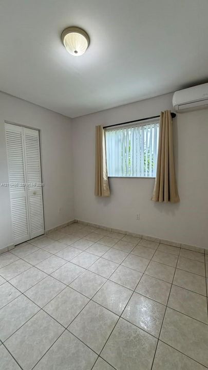 Ceramic tile flooring, wall-mounted ductless air conditioning unit, bi-fold closet doors, and flush-mount ceiling light fixture