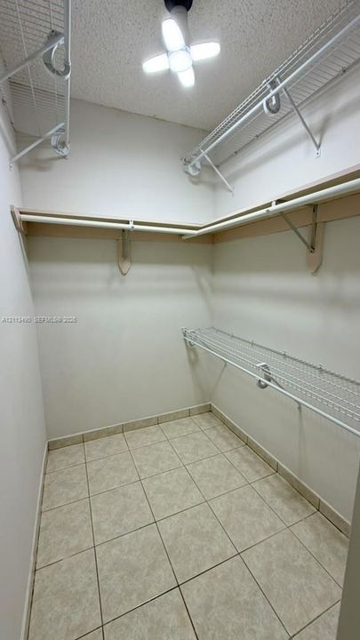 Walk-in storage space featuring multi-level wire shelving, a continuous rod, tiled flooring, and a multi-panel LED ceiling fixture