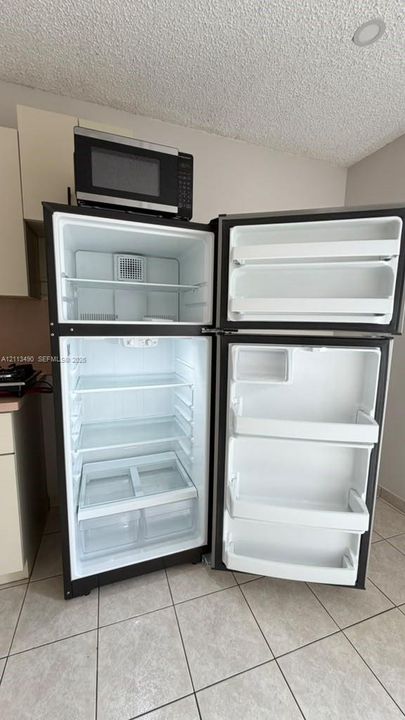 Top-mount stainless steel refrigerator with adjustable interior shelving, clear storage drawers, and door bins, featuring an integrated microwave above