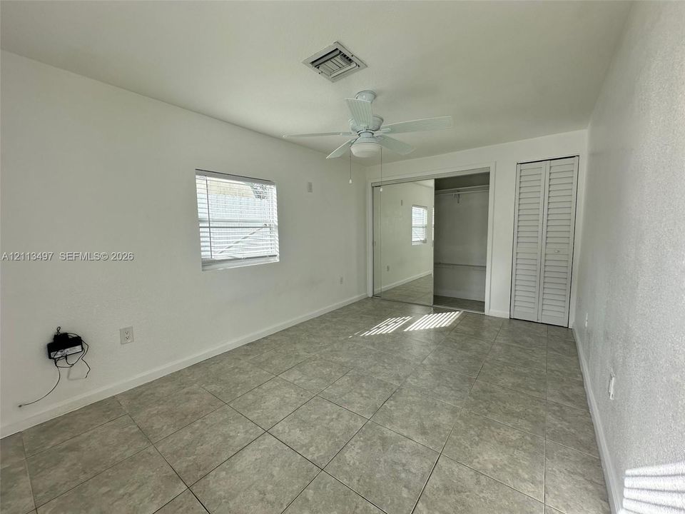 Neutral-toned tile flooring, white wall finish, ceiling fan with integrated lighting, sliding mirror-panel closet doors, and bi-fold closet doors