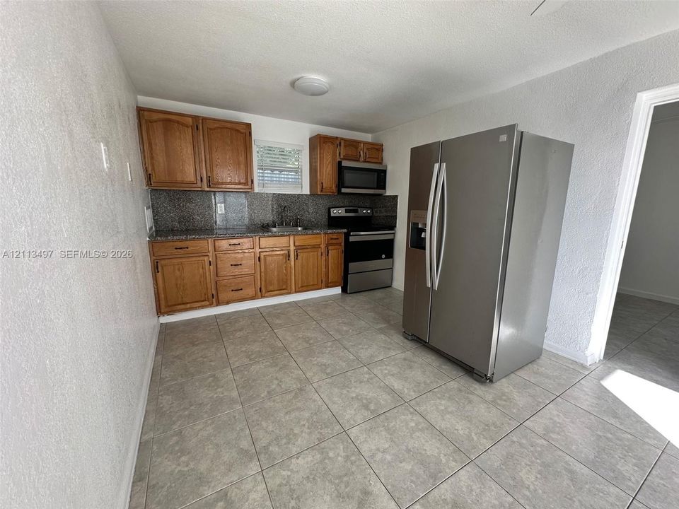 Kitchen featuring wood cabinetry, stone-finish countertops, tile flooring, and stainless steel appliances including a built-in microwave and refrigerator