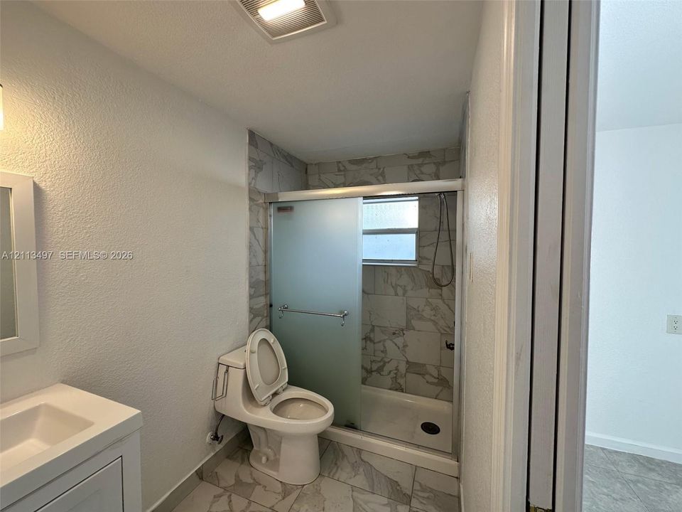 Bathroom featuring a shower stall with semi-frameless frosted glass doors, patterned wall tile, a one-piece elongated toilet, and a vanity with a white countertop