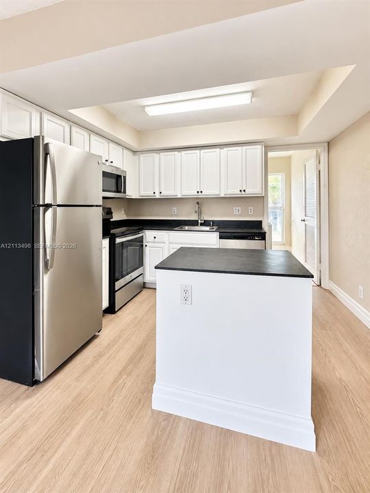 Kitchen featuring white cabinetry, contrasting dark countertops, stainless steel appliances, central island, and wood-finish flooring