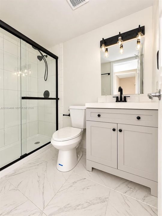 Bathroom featuring a walk-in shower with matte black hardware and a glass enclosure, light-toned cabinetry with a solid-surface vanity top, matte black faucet, and large-format tile flooring