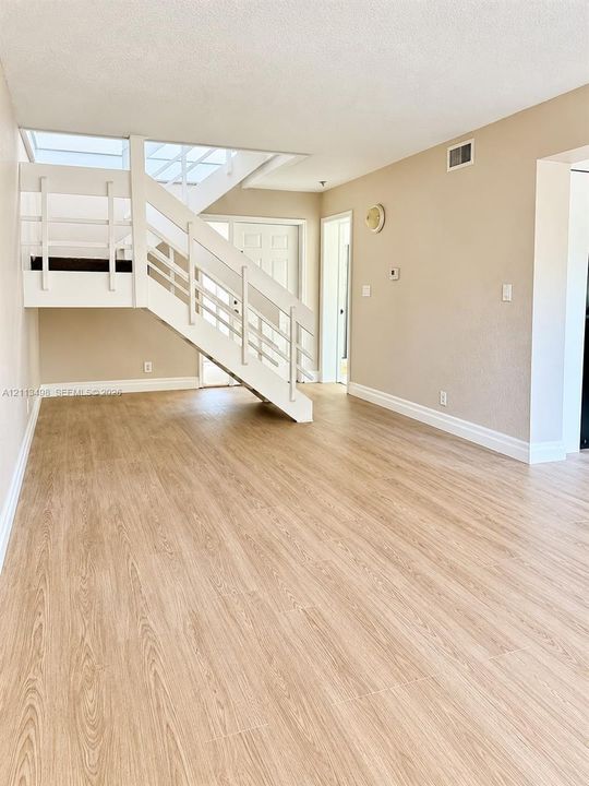 Open-concept interior featuring wood-finish flooring, a white structural staircase with horizontal railings, and a skylight