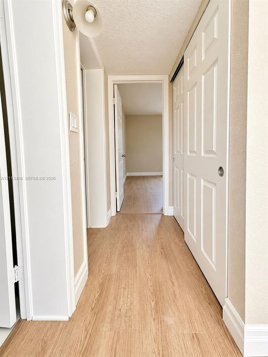 Hallway featuring wood-finish flooring, white panel interior doors, and a wall-mounted light fixture