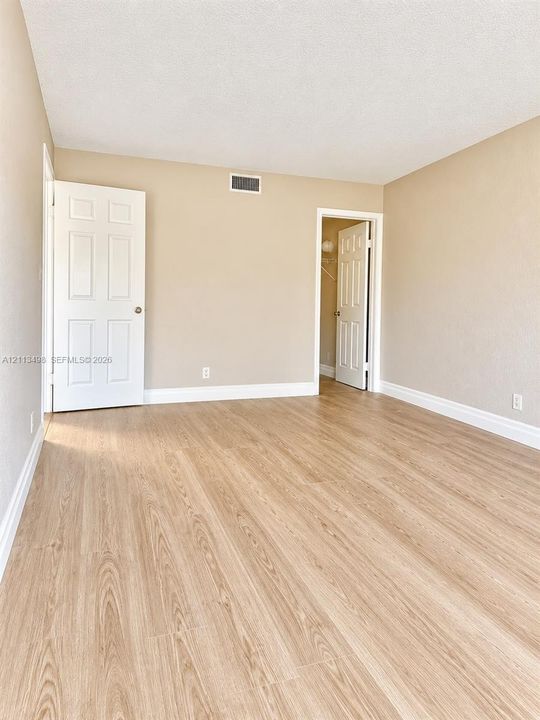 Neutral interior space featuring wood-finish flooring, white six-panel doors, and textured wall surfaces