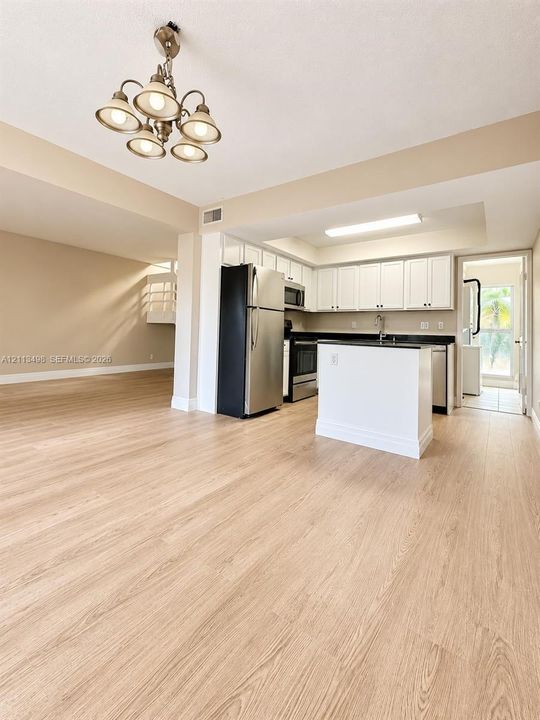 Kitchen featuring white shaker-style cabinetry, a central island with a solid-surface countertop, stainless steel appliances, and wood-finish flooring