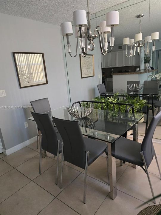 Dining area featuring neutral tile flooring, a wall-to-wall mirror installation, and a polished metal chandelier with white drum shades