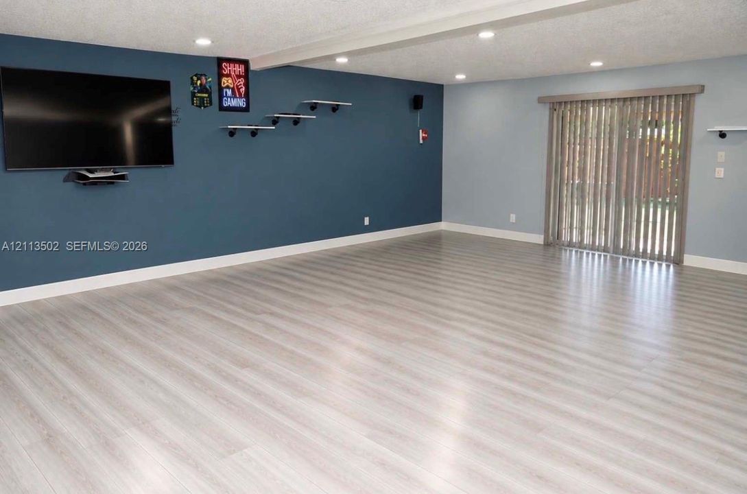 Interior space featuring wood-finish flooring, recessed lighting, a dark-toned accent wall with wall-mounted shelving, and sliding glass doors with vertical blinds