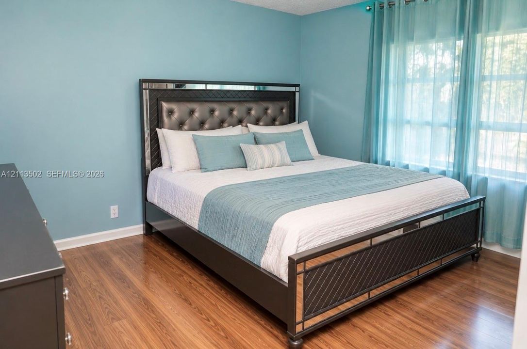 Wood-finish flooring throughout the room with multi-pane windows and sheer window treatments