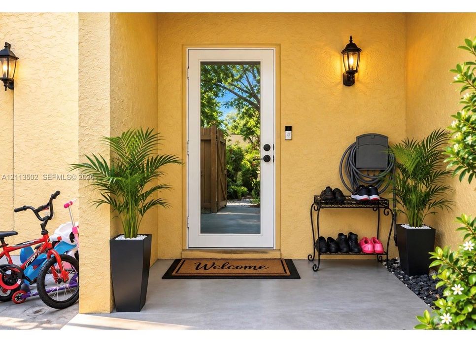 Covered entryway featuring stucco exterior walls, a full-length glass-panel door with matte black hardware, and two wall-mounted outdoor lanterns