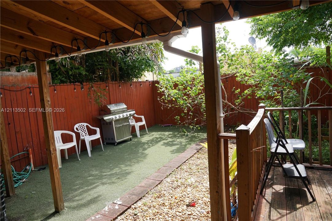 Covered patio with wood framing, synthetic turf ground cover, perimeter wood fencing, and natural gravel ground cover