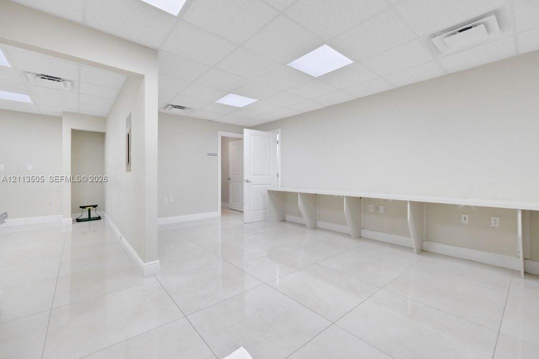 Spacious interior featuring large-format tile flooring, a suspended drop ceiling with recessed lighting panels, and a built-in custom desk surface
