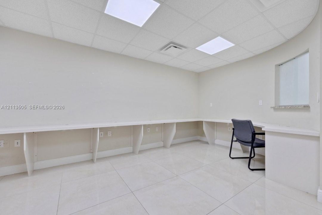 Custom wall-to-wall built-in desk, large-format tile flooring, drop ceiling with recessed lighting, and curved wall architecture