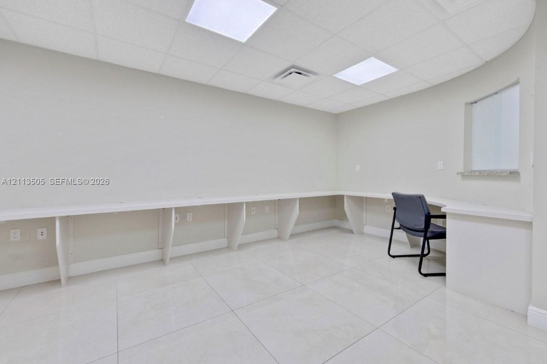 Expansive room featuring recessed drop-ceiling lighting, polished tile flooring, a wrap-around built-in desk with stone countertop, and an interior service window