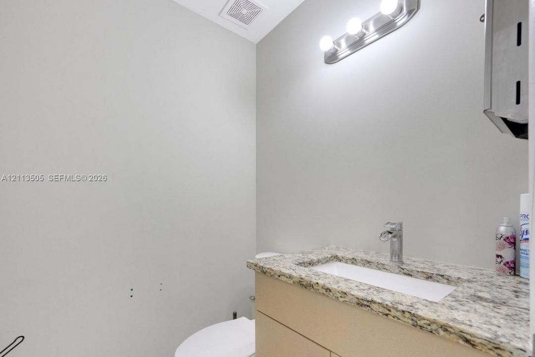 Neutral-toned vanity featuring a stone-finish countertop, undermount sink, chrome faucet, and integrated lighting fixture