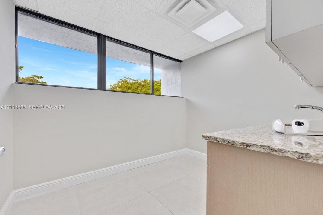 Interior space featuring large-pane windows, a stone-surfaced countertop, built-in cabinetry, an integrated sink with a chrome faucet, and tile flooring