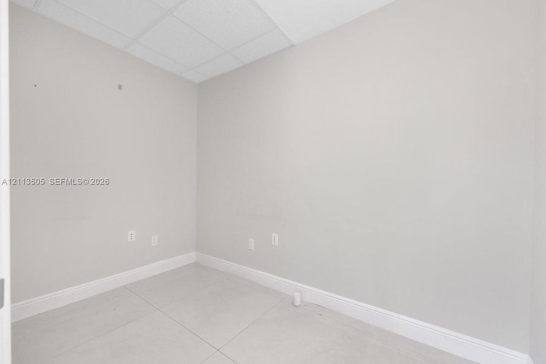 Neutral-toned room featuring large-format tile flooring and drop ceiling panels