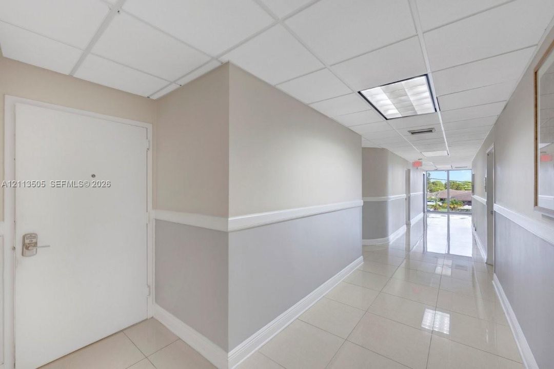 Hallway featuring neutral two-tone wall paint, white chair rail trim, large-format tile flooring, and a suspended drop ceiling with recessed lighting
