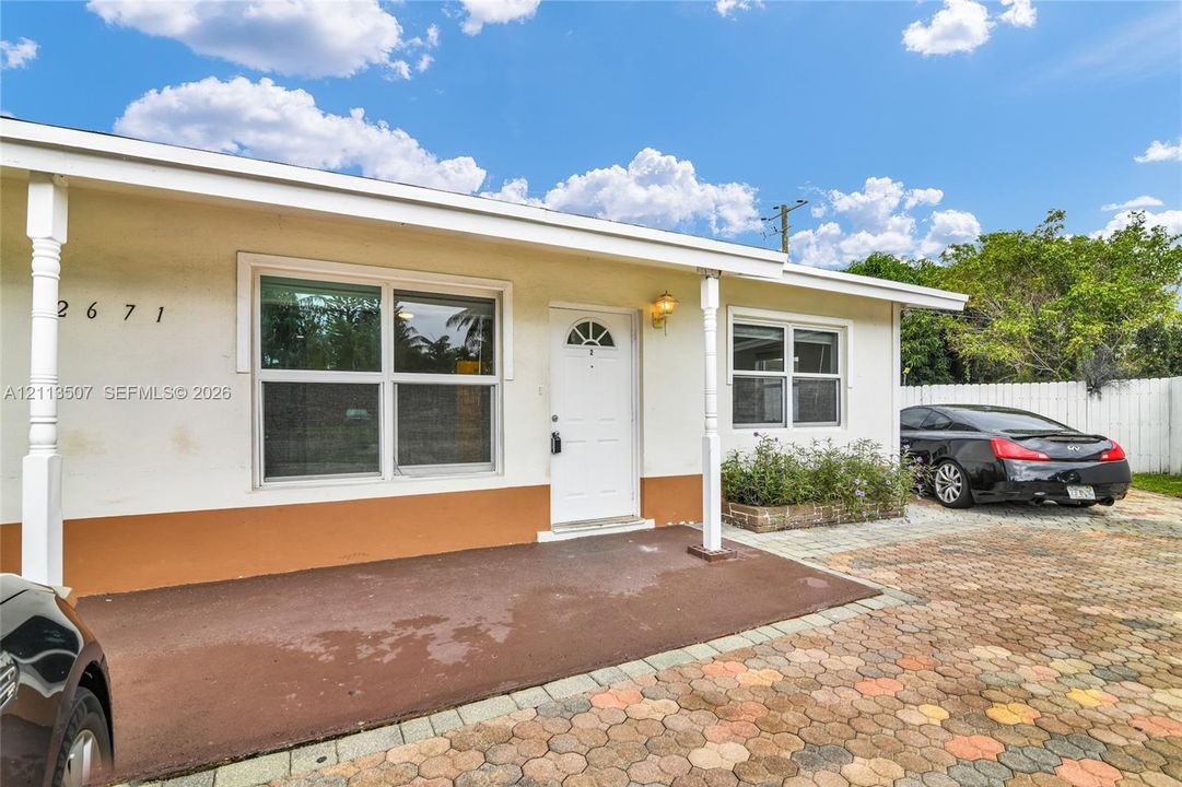 Exterior facade featuring stucco siding, a covered front porch, multi-pane windows, and a paved brick driveway