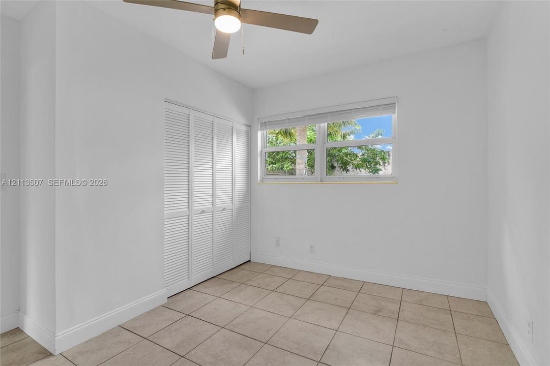 Tile flooring, built-in louvered-panel closet doors, and a ceiling fan with integrated lighting