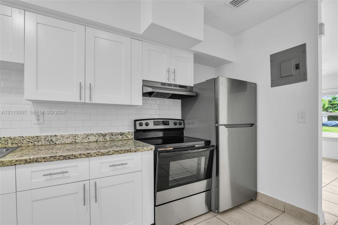 Kitchen featuring white Shaker-style cabinetry, stone countertops, a white subway tile backsplash, and stainless steel appliances