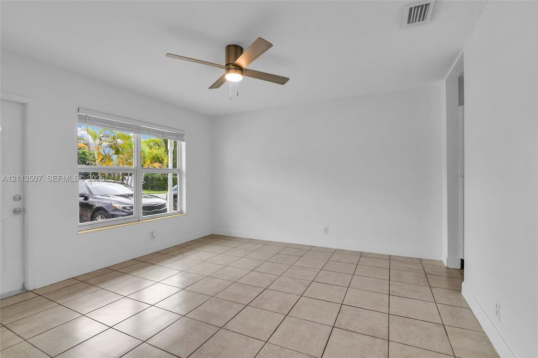 Neutral interior space featuring tile flooring, a metallic ceiling fan with integrated lighting, and large windows