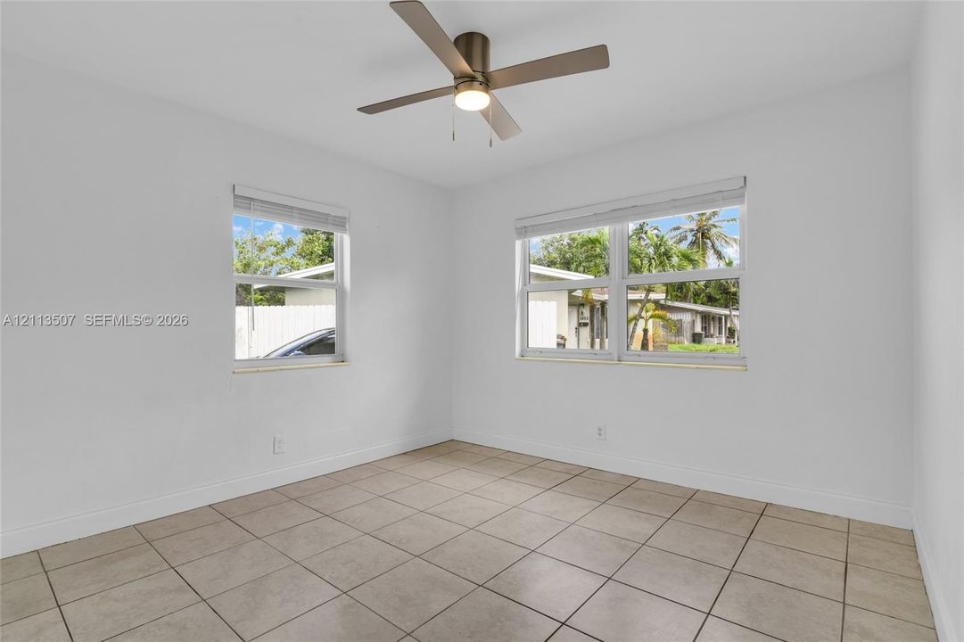 Neutral-toned ceramic tile flooring, metallic ceiling fan with integrated lighting, and dual windows with horizontal blinds