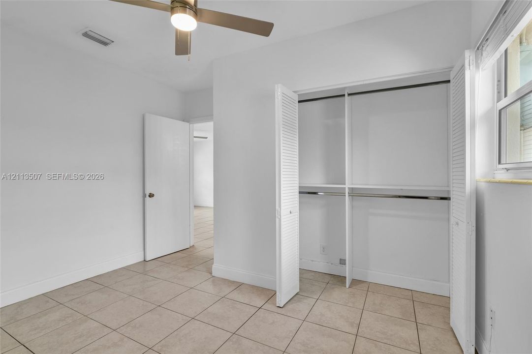 Neutral-toned ceramic tile flooring, closet with bi-fold louvered doors, ceiling fan with integrated lighting, and window with horizontal blinds