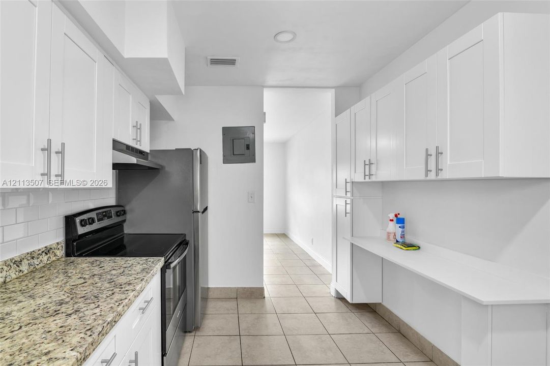 Kitchen featuring white shaker-style cabinetry, stone-finish countertops, subway tile backsplash, stainless steel appliances, and ceramic tile flooring